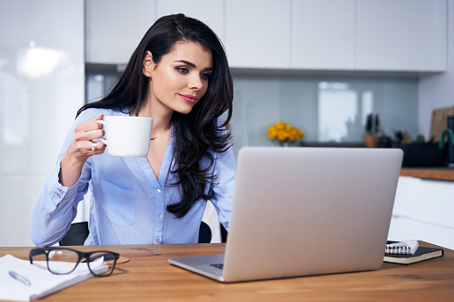 Woman working on laptop and drinking coffee in home office